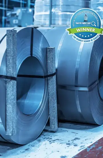 Rolls of steel in a manufacturing facility with a Search Engine Land award badge, representing industrial marketing success.