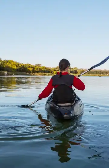 Person kayaking on a calm river surrounded by trees, representing exploration and paid search discovery strategies.