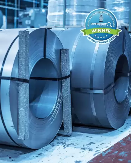 Rolls of steel in a manufacturing facility with a Search Engine Land award badge, representing industrial marketing success.