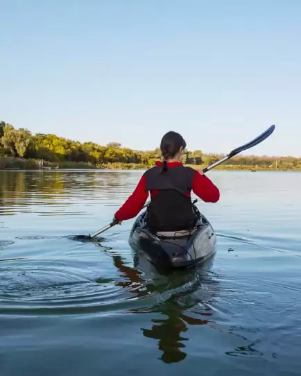 Person kayaking on a calm river surrounded by trees, representing exploration and paid search discovery strategies.