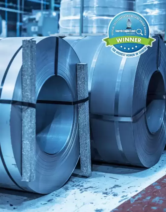 Rolls of steel in a manufacturing facility with a Search Engine Land award badge, representing industrial marketing success.